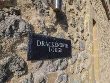 A black sign reading Drackenorth Lodge on a stone wall with a small light above it at Stapleford Farm in Hooke near Beaminster