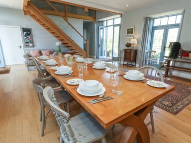 A dining room with a large wooden table set for a meal with chairs around it and wooden stairs in the background at Stapleford Farm in Hooke near Beaminster