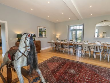 A dining room with a long set table and chairs and a rocking horse on a rug at Stapleford Farm in Hooke near Beaminster