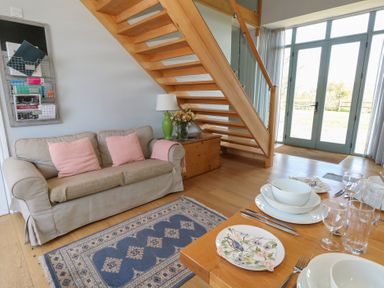 A living area with a sofa near wooden stairs and a dining table set with plates and glasses at Stapleford Farm in Hooke near Beaminster