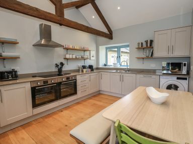 A kitchen with wooden beams double ovens a dining table a green chair and a washing machine at Stapleford Farm in Hooke near Beaminster