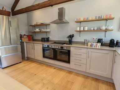 A kitchen with wooden floors double ovens shelves with dishes and mugs and a stainless steel refrigerator at Stapleford Farm in Hooke near Beaminster