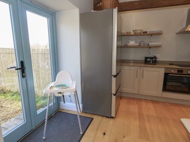 A kitchen with a high chair by blue glass doors a silver refrigerator wooden floor and shelves with dishes at Stapleford Farm in Hooke near Beaminster