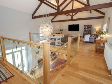 An upstairs sitting area with wooden floors wooden beams a chandelier foosball table and glass railing at Stapleford Farm in Hooke near Beaminster