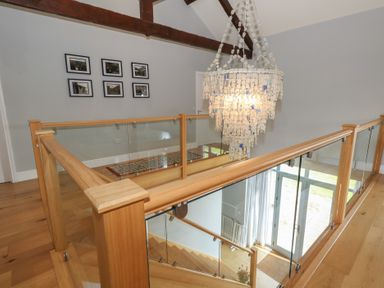 An upstairs hallway with wooden floor glass railing and a chandelier at Stapleford Farm in Hooke near Beaminster