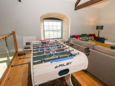 A foosball table beside sofas with cushions and a lamp in a room with a window and wooden beams at Stapleford Farm in Hooke near Beaminster