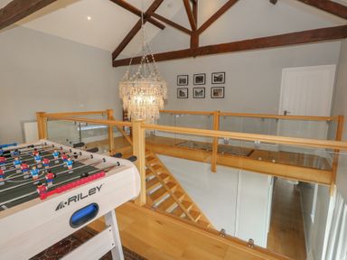 A loft area with a foosball table wooden railing glass panels wooden beams and a chandelier at Stapleford Farm in Hooke near Beaminster