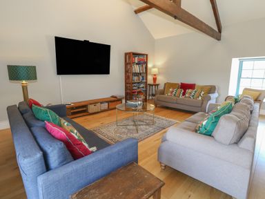 A living room with sofas cushions a wall-mounted TV and a bookshelf at Stapleford Farm in Hooke near Beaminster