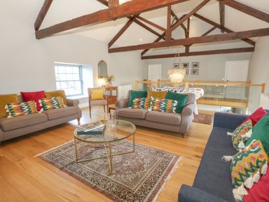 A sitting area with sofas and colorful pillows a glass coffee table and exposed wooden beams at Stapleford Farm in Hooke near Beaminster