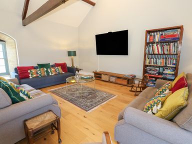 A living room with sofas cushions a glass coffee table a television and a bookshelf at Stapleford Farm in Hooke near Beaminster