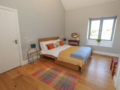 A bedroom with a wooden bed a glass side table with a lamp a small red table and chair a window with flowers on the sill and a colorful rug on wooden floor at Stapleford Farm Hooke near Beaminster
