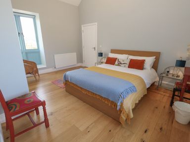 A bedroom with a bed pillows and blankets a wooden floor two chairs a window and bedside tables at Stapleford Farm in Hooke near Beaminster