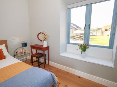 A bedroom with a bed a side table with a lamp a small red dressing table with a mirror and stool and a window with flowers on the sill at Stapleford Farm in Hooke near Beaminster