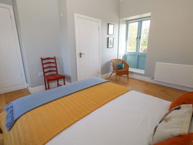 A bedroom with a bed a blue and yellow blanket a red chair a wicker chair with a cushion two framed pictures on the wall and a window at Stapleford Farm Hooke near Beaminster