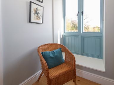 A corner with a wicker chair with a blue cushion next to a window with blue shutters and framed artwork on the wall at Stapleford Farm in Hooke near Beaminster