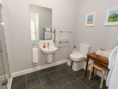 A bathroom with a sink mirror toilet wooden table stool and wall art at Stapleford Farm in Hooke near Beaminster
