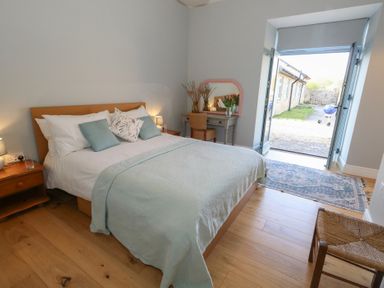 A bedroom with a bed bedside tables a dressing table chair and open double doors leading outside at Stapleford Farm in Hooke near Beaminster