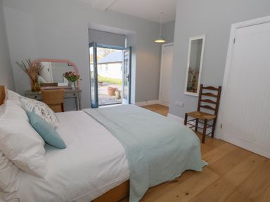 A bedroom with a bed a vanity table with flowers a chair a door and wooden flooring at Stapleford Farm in Hooke near Beaminster