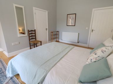A bedroom with a bed with pillows and a blanket two doors a chair a wall mirror and a framed picture at Stapleford Farm in Hooke near Beaminster