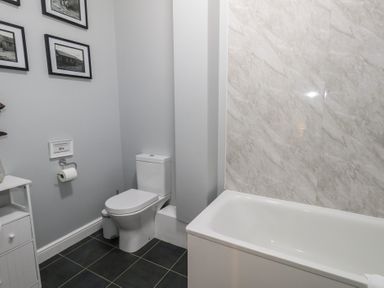 A bathroom with a toilet next to a bathtub and framed pictures on the wall at Stapleford Farm in Hooke near Beaminster