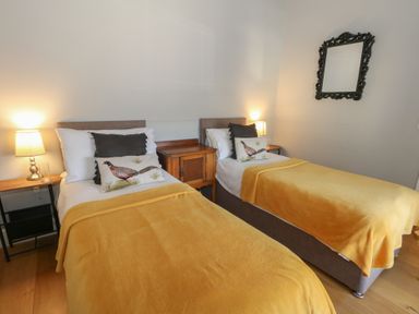 A bedroom with two single beds with yellow blankets pillows with bird designs a wooden nightstand and lamps at Stapleford Farm in Hooke near Beaminster