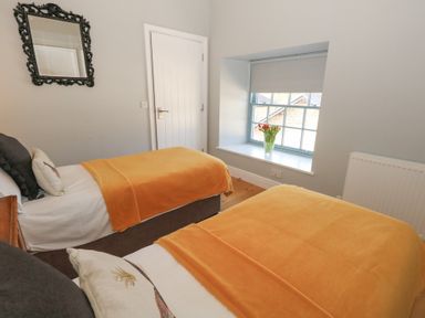 A bedroom with two single beds with orange blankets a window with flowers a door a mirror and a radiator at Stapleford Farm in Hooke near Beaminster