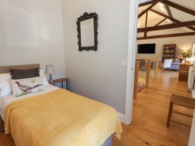A bedroom with a yellow bedspread and decorative pillows next to a side table with a lamp and an ornate mirror on the wall overlooking a living area with exposed wooden beams at Stapleford Farm Hooke near Beaminster