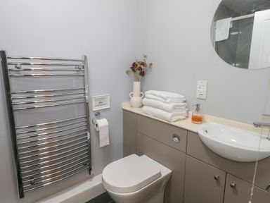 A bathroom with a toilet, a wall-mounted sink, a round mirror, a towel radiator, and folded towels on a countertop at Stapleford Farm in Hooke near Beaminster