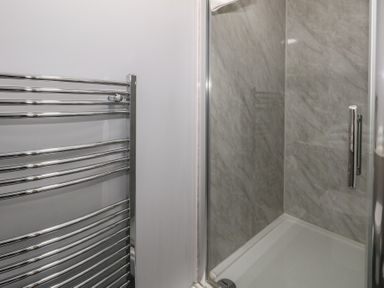 A shower with glass door and tiled walls next to a chrome towel radiator in a bathroom at Stapleford Farm in Hooke near Beaminster