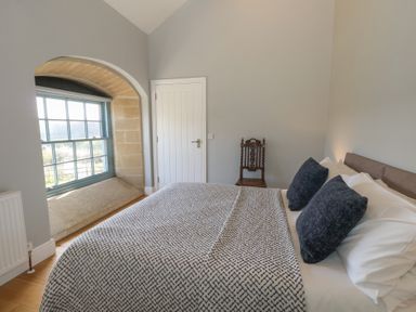 A bedroom with a patterned bedspread two pillows wooden chair and a window with a stone frame at Stapleford Farm in Hooke near Beaminster
