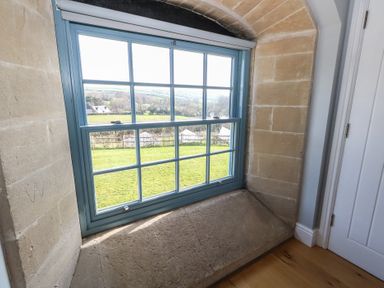 A window with blue frame and stone windowsill overlooking a green field at Stapleford Farm in Hooke near Beaminster