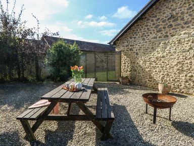 An outdoor patio with a wooden picnic table flowers and tea set a fire pit and a stone wall at Stapleford Farm in Hooke near Beaminster