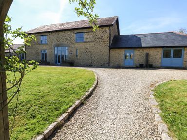 A stone building with blue doors and windows and a gravel driveway at Stapleford Farm in Hooke near Beaminster