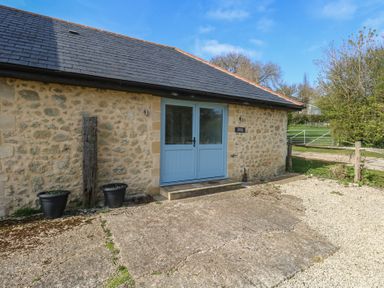 Stone building with blue double doors two black plant pots and a gravel driveway at Stapleford Farm in Hooke near Beaminster