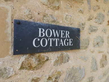 A black sign with white letters saying Bower Cottage on a stone wall