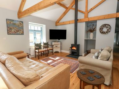 A living room with exposed wooden beams a leather sofa fabric armchair wood burning stove and television at Stapleford Farm in Hooke near Beaminster
