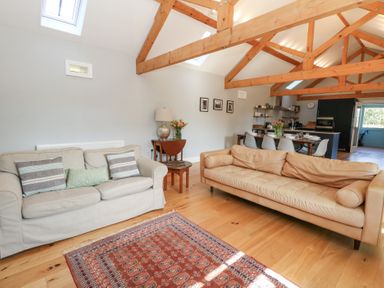 A living room with two sofas a wooden floor a rug exposed wooden beams and a dining area at Stapleford Farm in Hooke near Beaminster