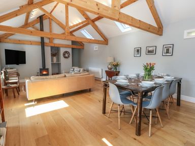 An open living and dining room with exposed wooden beams a fireplace a beige sofa and a dining table set with dishes at Stapleford Farm in Hooke near Beaminster
