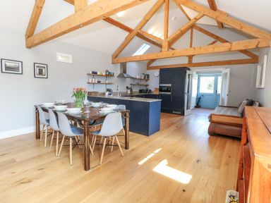 A dining area with a wooden table set for six and a kitchen with blue cabinets and exposed wooden beams at Stapleford Farm in Hooke near Beaminster