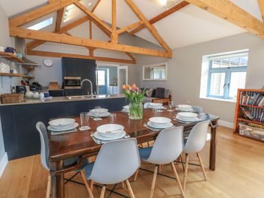 A dining table with chairs and tableware in an open kitchen and living space with wooden beams at Stapleford Farm in Hooke near Beaminster