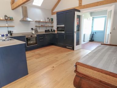 A kitchen with blue cabinets wooden floors open doorway and a wooden bed at Stapleford Farm in Hooke near Beaminster