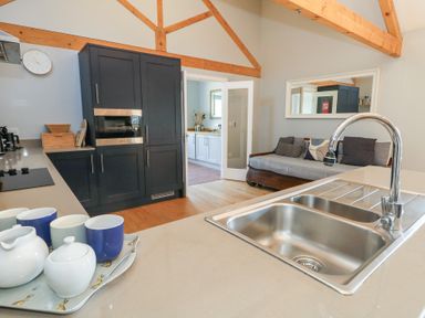 A kitchen area with a sink faucet cups on a tray and a sofa with cushions at Stapleford Farm in Hooke near Beaminster