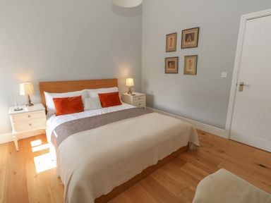 A bedroom with a double bed with white pillows and orange cushions two bedside tables with lamps wooden floor and framed pictures on the wall at Stapleford Farm Hooke near Beaminster