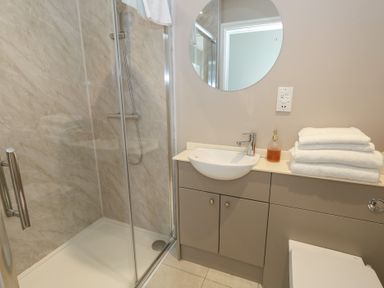 A bathroom with a shower enclosure a sink with a faucet a round mirror and folded towels on a countertop at Stapleford Farm in Hooke near Beaminster