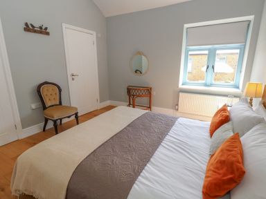 A bedroom with a bed orange pillows a chair a round mirror and a window at Stapleford Farm in Hooke near Beaminster