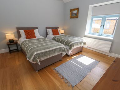 A bedroom with two single beds a bedside table with a lamp a window and a rug on the wooden floor at Stapleford Farm in Hooke near Beaminster