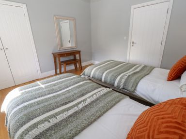 A bedroom with two single beds with striped blankets orange pillows a wooden table with a bench and a wall mirror at Stapleford Farm in Hooke near Beaminster