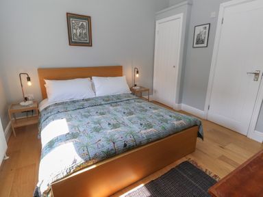 A bedroom with a wooden bed, bedside tables with lamps, artwork on the walls and wooden flooring at Stapleford Farm in Hooke near Beaminster