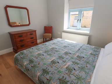 A bedroom with a bed covered with a patterned quilt a wooden dresser with mirror a chair by the window at Stapleford Farm in Hooke near Beaminster