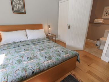 A bedroom with a wooden bed and bedding with animal and tree pattern and an open door to a bathroom at Stapleford Farm in Hooke near Beaminster